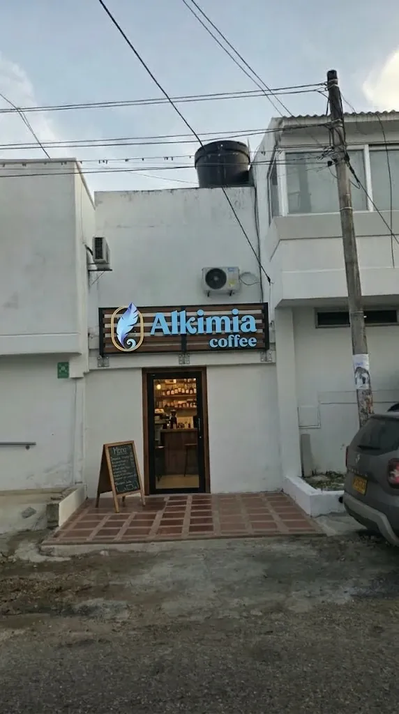 Fachada de Alkimia Coffee: puerta de madera y vidrio bajo el letrero con la pluma azul